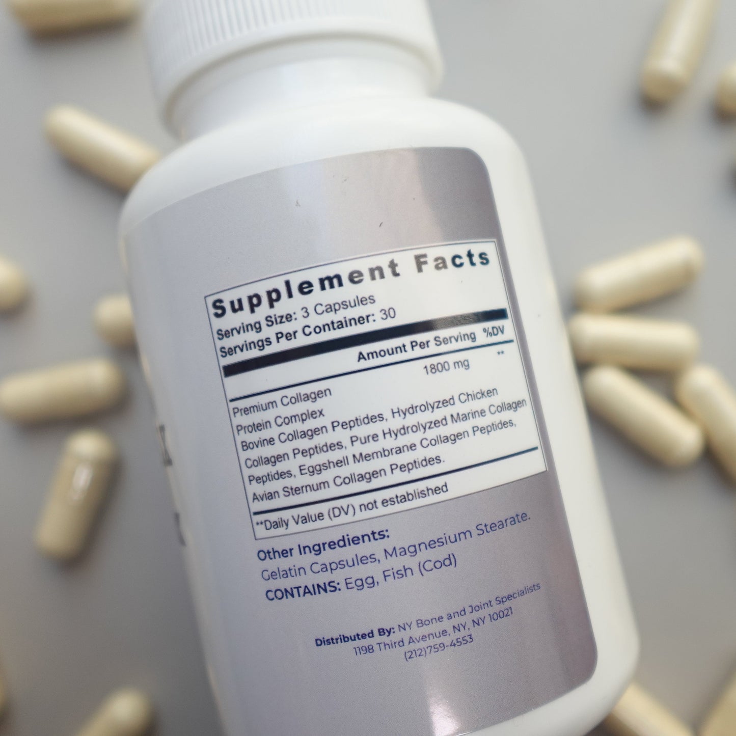 Supplement bottle with label surrounded by capsules on a gray background