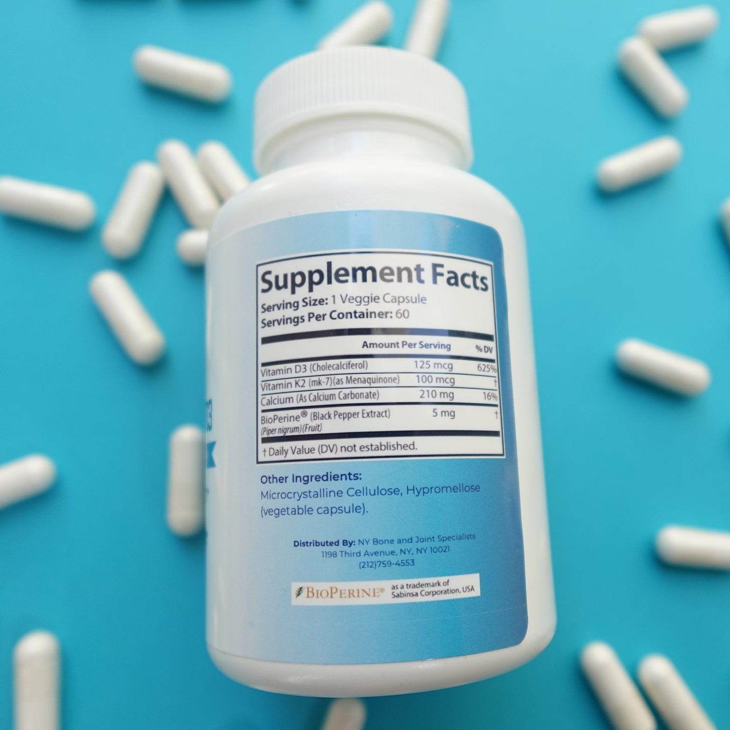Supplement bottle with 'Supplement Facts' label on a blue background with scattered white capsules.
