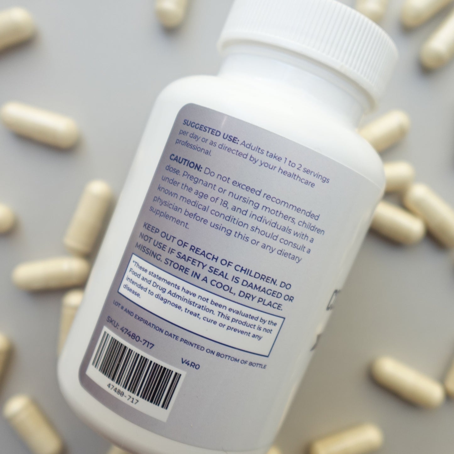 White pill bottle with label and bar code on a gray background with scattered pills.